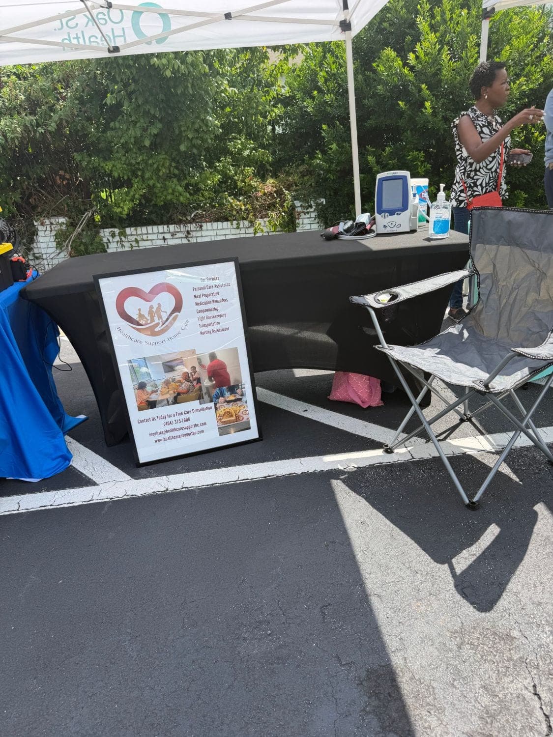 Healthcare Support Home Care's table with a blood pressure monitor and services poster, offering free blood pressure checks at the Oak Street Health East Point food pantry outreach